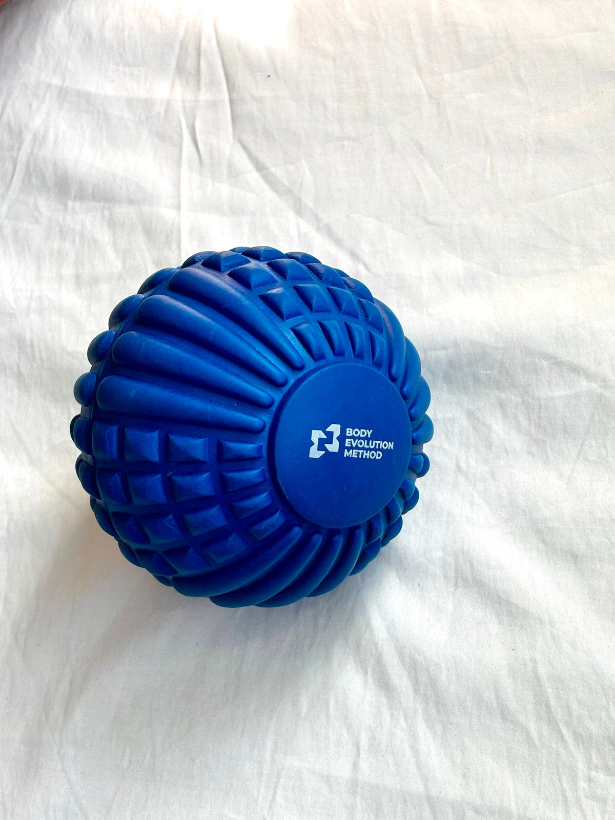 Blue textured Psoas Ball with Body Evolution Method logo, held in hand